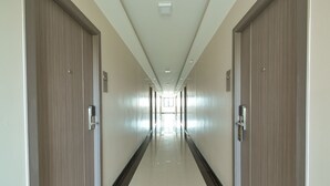Un long couloir étroit, bordé de portes en bois de chaque côté, qui mène à un espace lumineux au fond.