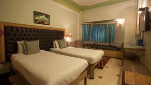 A hotel room with two beds, a sofa, a television, and a window with curtains. - Hotel Samrat International (Patna)