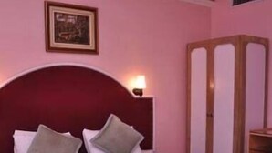 A bedroom with a large bed, a wooden headboard, a bedside table, and a framed picture on the wall. - Hotel Samrat International (Patna)
