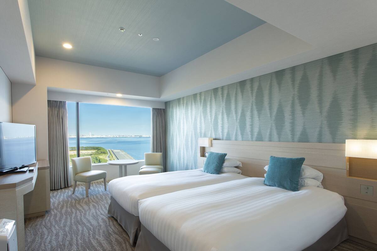 Habitación de hotel con dos camas, un televisor, un escritorio y vista al mar.