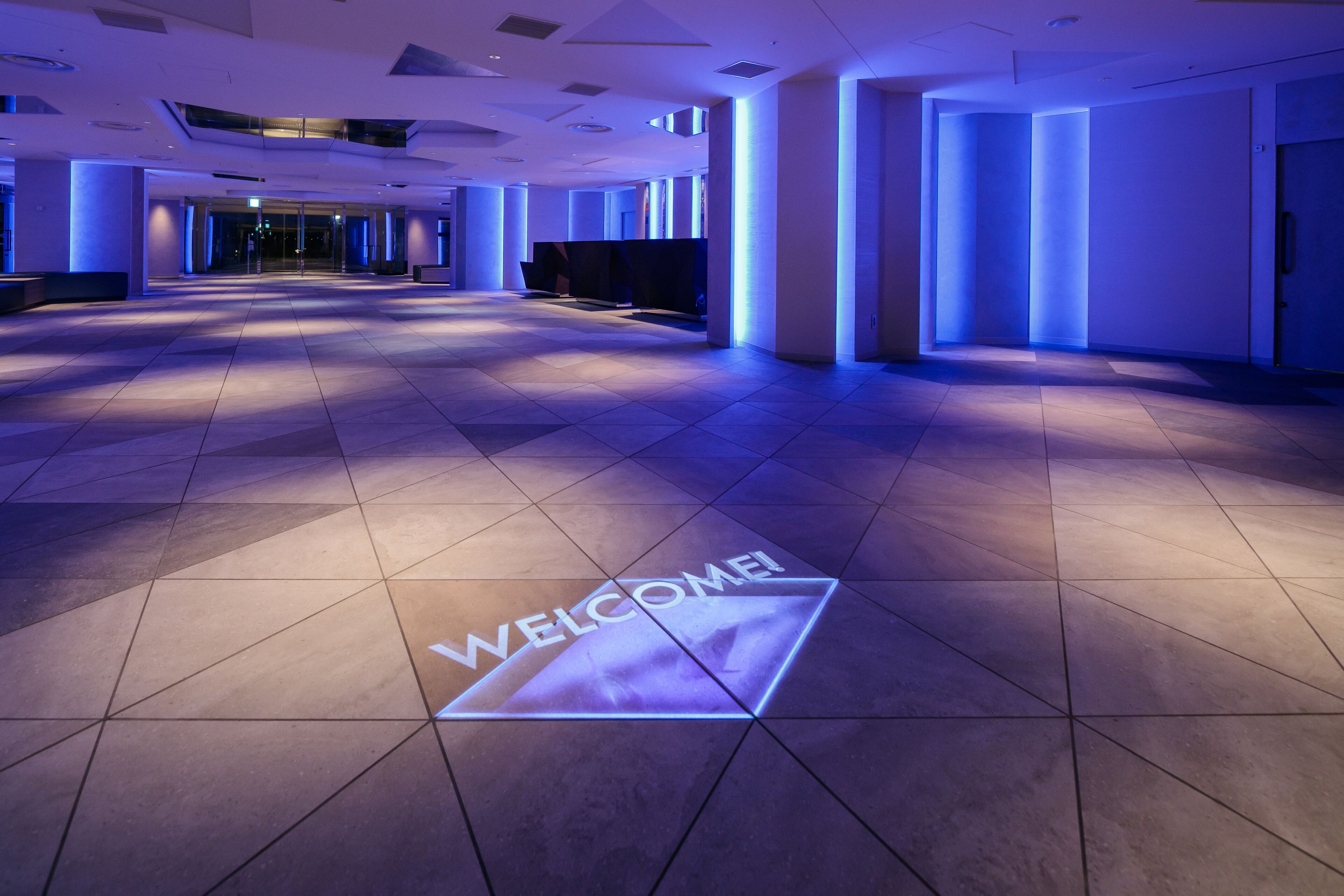 A spacious lobby with a 'WELCOME' floor projection, modern lighting, and a clean, contemporary design.
