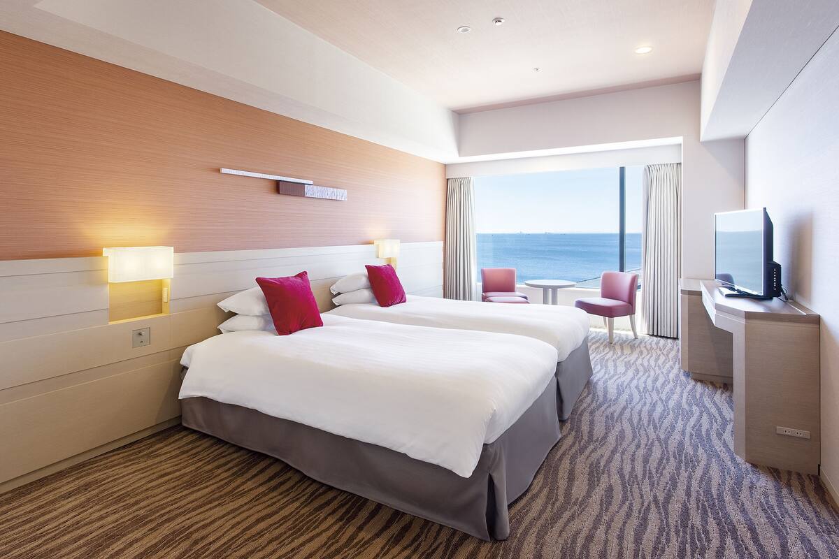 Habitación de hotel con dos camas, televisión, escritorio y vista al mar.