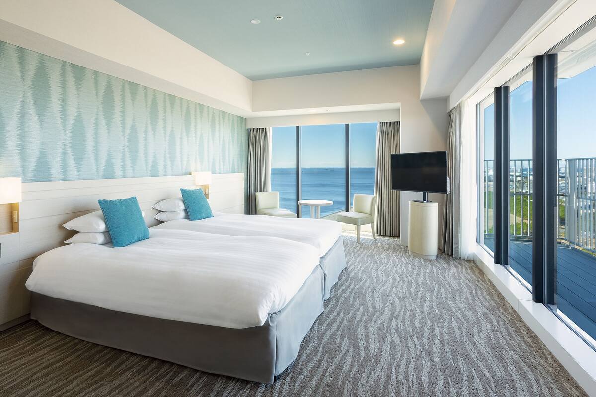Habitación de hotel con una cama grande, televisión, una mesita y vista al océano.