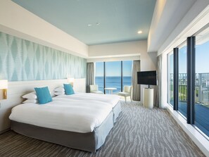 A hotel room with a large bed, a TV, a small table, and a view of the ocean.