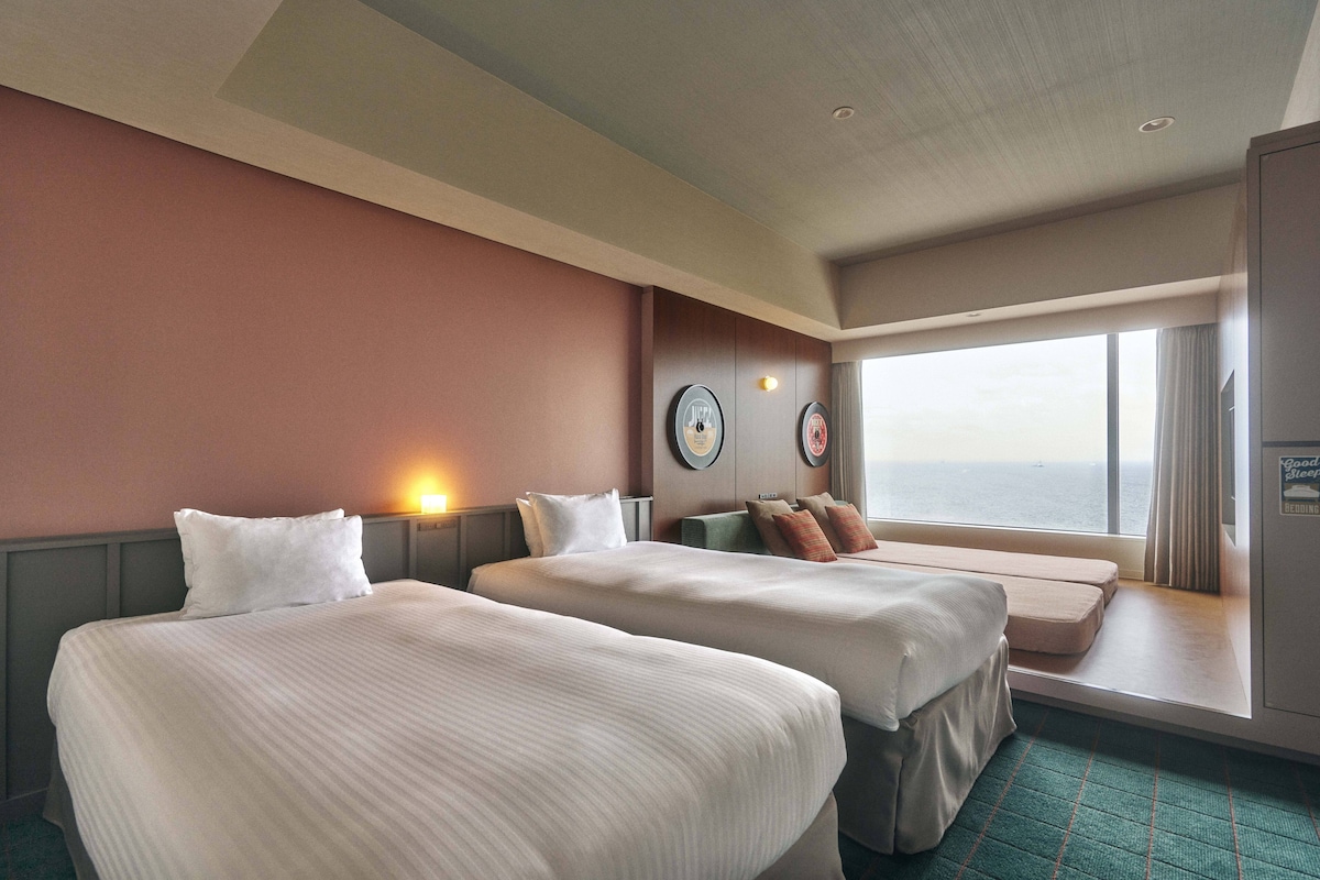Een hotelkamer met twee bedden, een zithoek met uitzicht en een groot raam.
