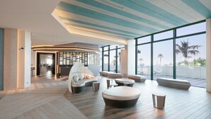 Ein stilvoller Lounge-Bereich mit gebogenen Sitzmöglichkeiten, großen Fenstern und Blick auf Palmen sowie einem Holzboden.