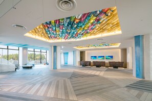 A spacious lobby with a modern design, featuring a unique ceiling installation, a reception area with seating, and large windows providing natural light.