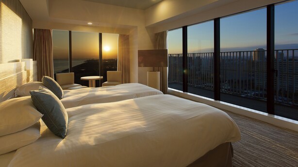 Ein Hotelzimmer mit zwei Betten, Blick auf die Stadt und einem Balkon mit Geländer.