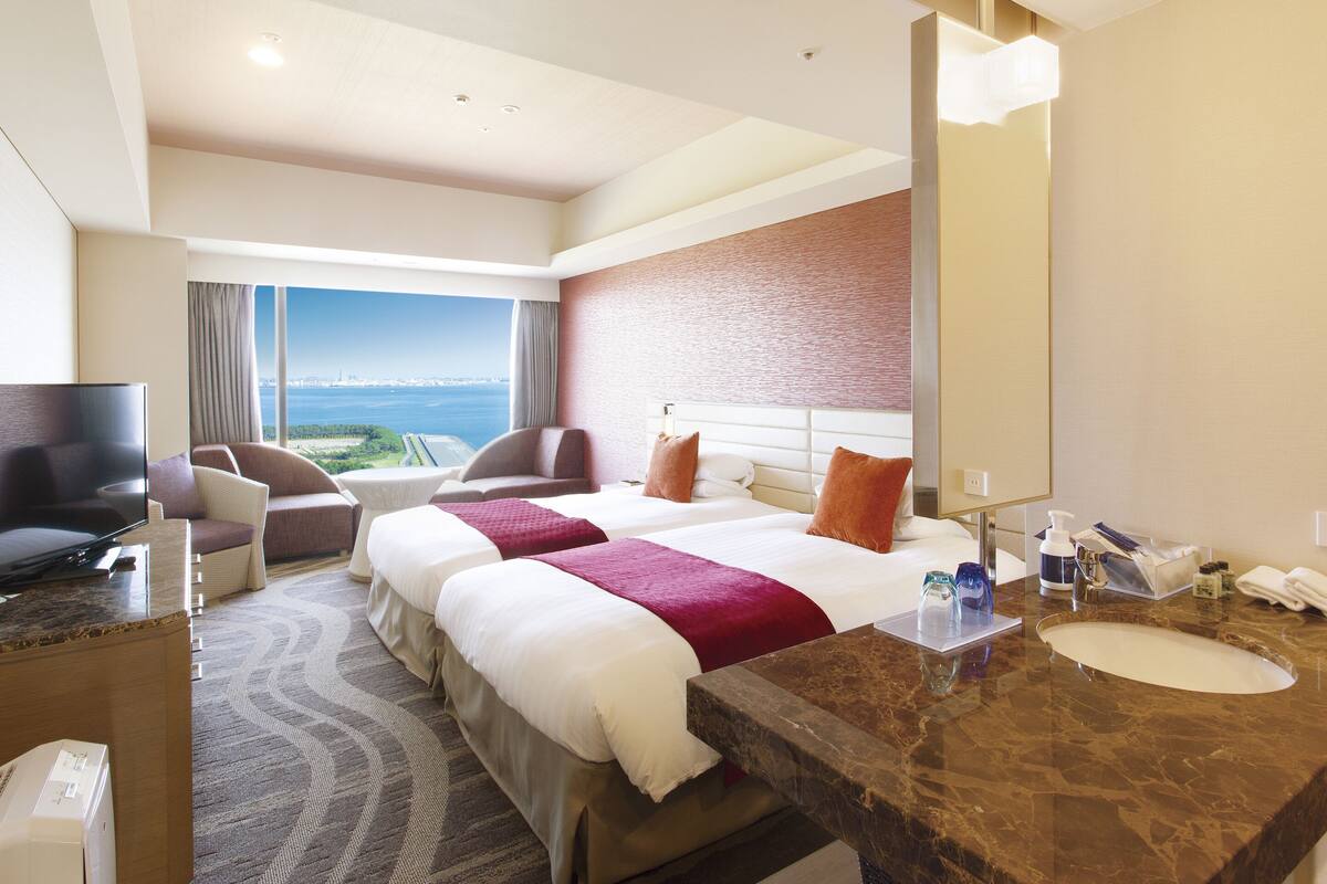 Habitación de hotel con una cama grande, zona de estar con vistas, televisor y baño con lavabo y espejo.
