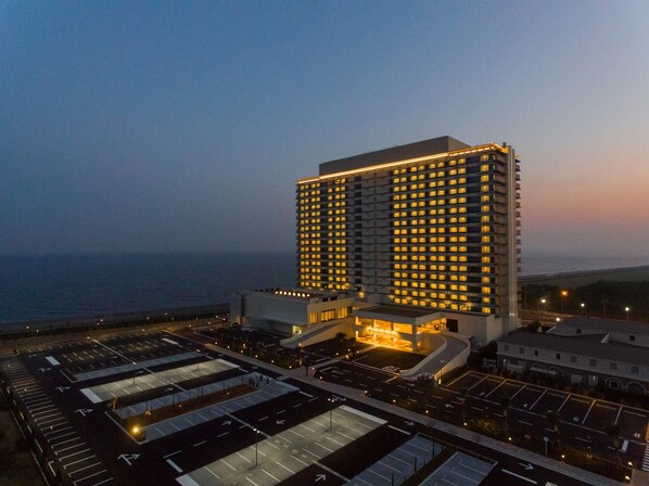 A high-rise hotel with multiple floors, a parking lot, and a view of the ocean.
