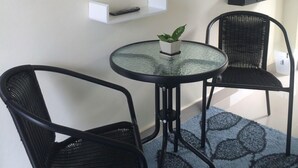 A small room with a TV mounted on the wall, a round table with two chairs, a small shelf, and a decorative mirror. - Baan  Kalaya Garden (Thep Krasattri)