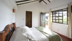 A bedroom with a wooden bed, a window with curtains, and a door. - Hospederia La Fuente (Villa de Leyva)