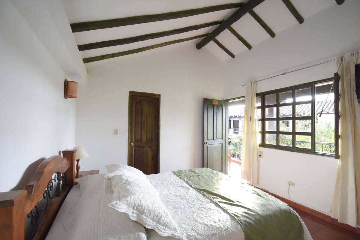 A bedroom with a wooden bed, a window with curtains, and a door.