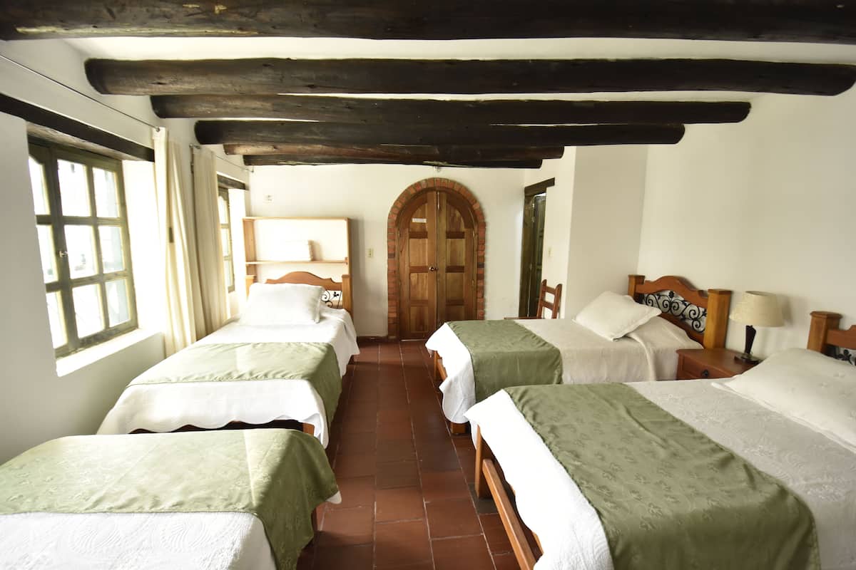 A room with four single beds, wooden headboards, a large arched wooden door, and a window with curtains.