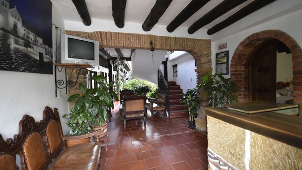 A traditional interior with a wooden bench, a TV, and a staircase leading to a second floor. - Hospederia La Fuente (Villa de Leyva)