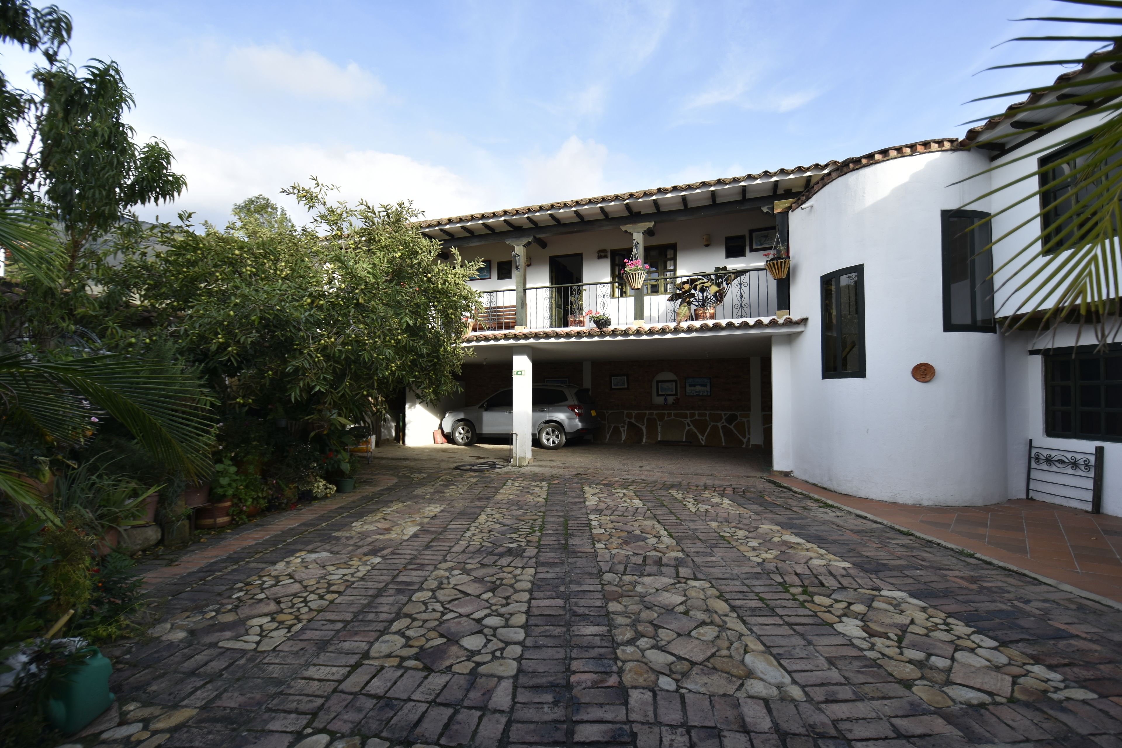 Un patio con un sendero adoquinado, un edificio blanco con tejado de azulejos y un coche estacionado.