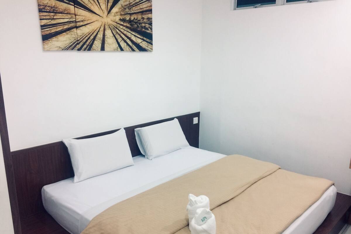 A neatly made bed with a beige blanket and two pillows, a wooden headboard, and a wall-mounted artwork.