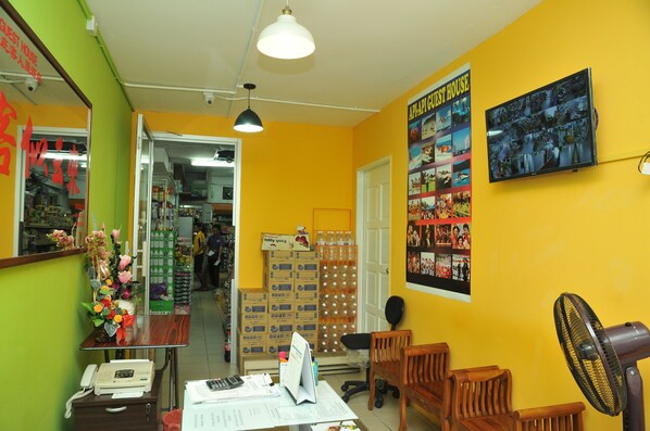 A room with a yellow wall, a wooden desk, a telephone, a chair, and a fan. - Api-Api Guest House (Kota Kinabalu)