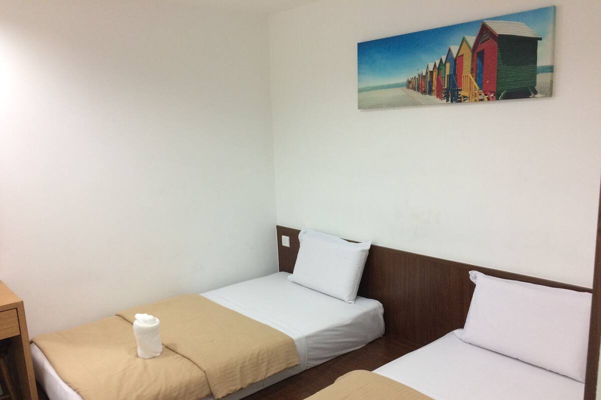 A hotel room with two single beds, a wooden headboard, a painting of colorful beach huts, and a wooden nightstand.