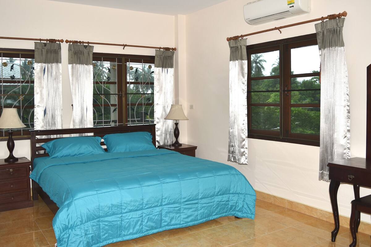 Um quarto com uma cama, duas mesas de cabeceira, uma luminária e cortinas em duas janelas.