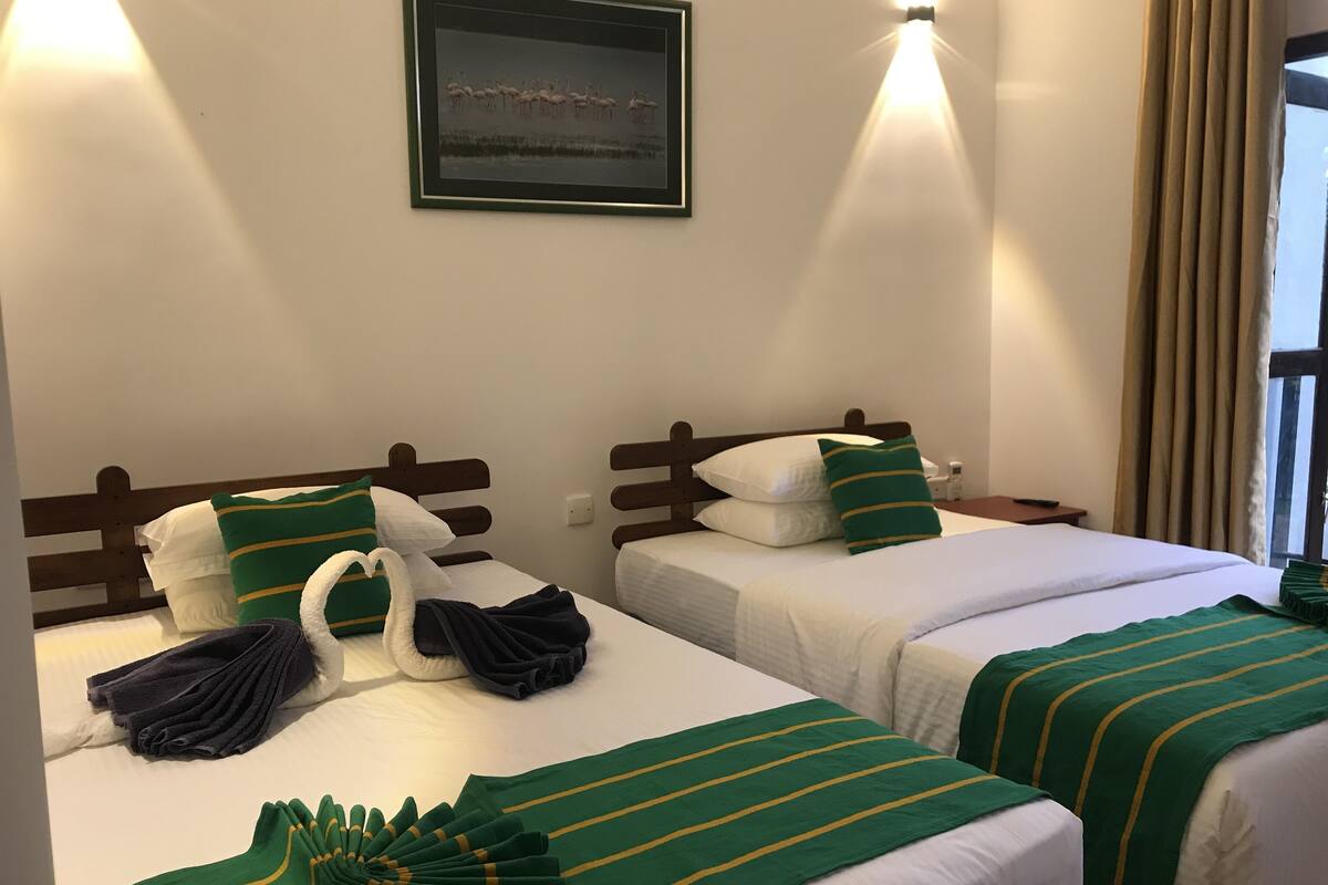 Een hotelkamer met twee bedden, elk met witte lakens en groene gestreepte dekens. Daarboven hangt een ingelijst foto aan de muur.
