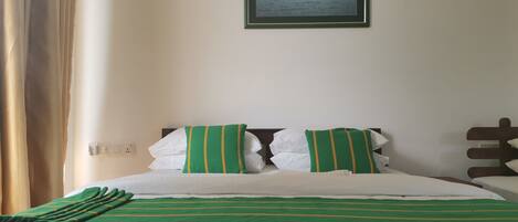 Una cama bien hecha con ropa de cama verde y blanca, un cuadro enmarcado de flamencos en la pared y un enchufe en la pared.