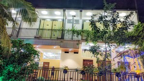 A multi-story building with balconies, a well-lit entrance, and a fenced garden area.