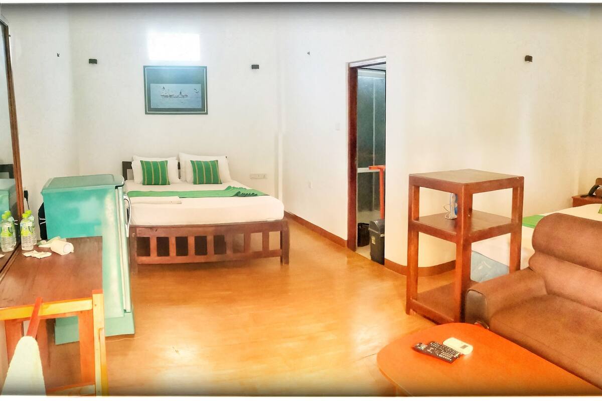 Een hotelkamer met een bed, een bank, een kleintje tafeltje, een televisie en een deur naar een andere kamer.