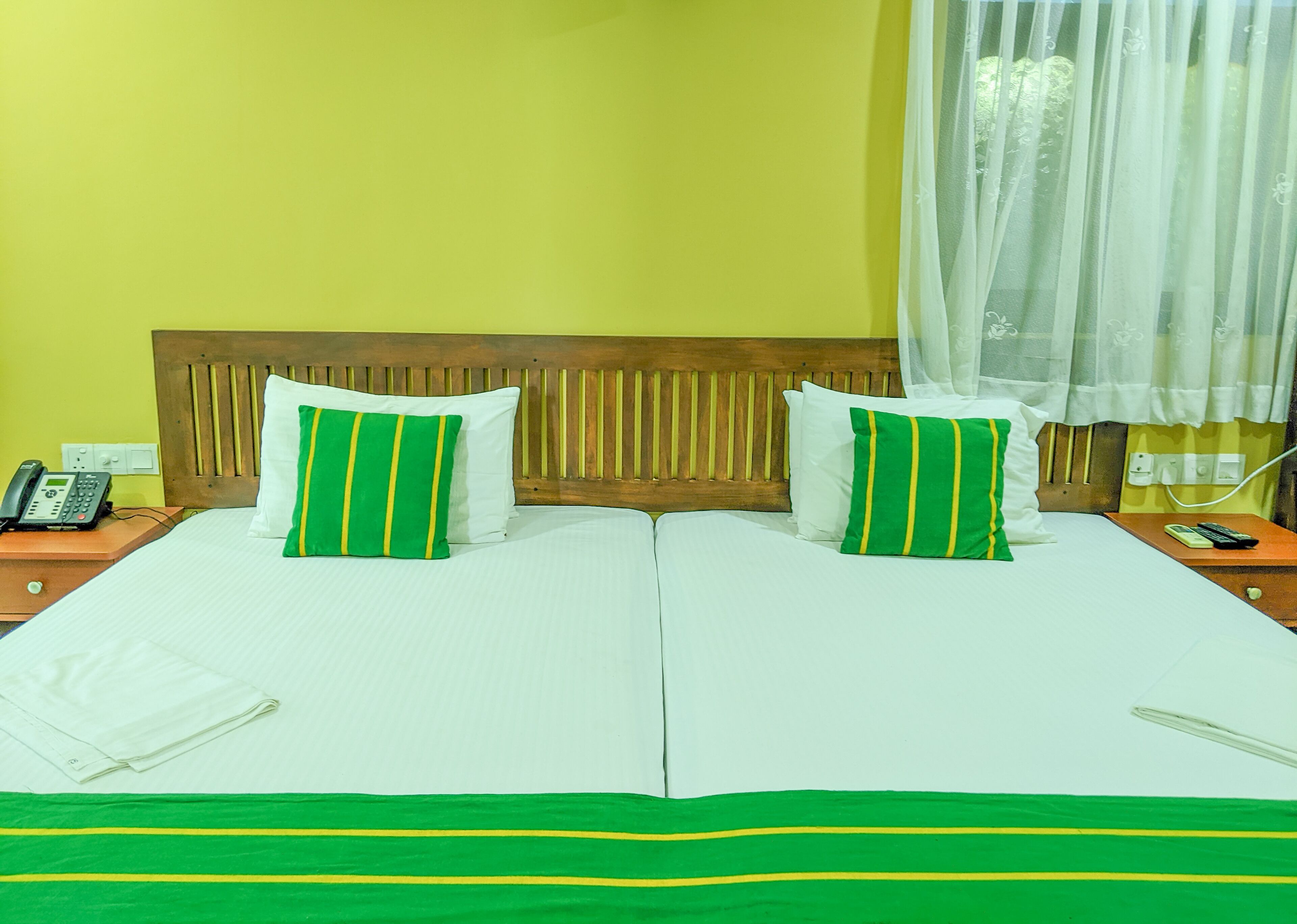 A hotel room with two beds, a wooden headboard, a telephone, and a bedside table with a remote control.
