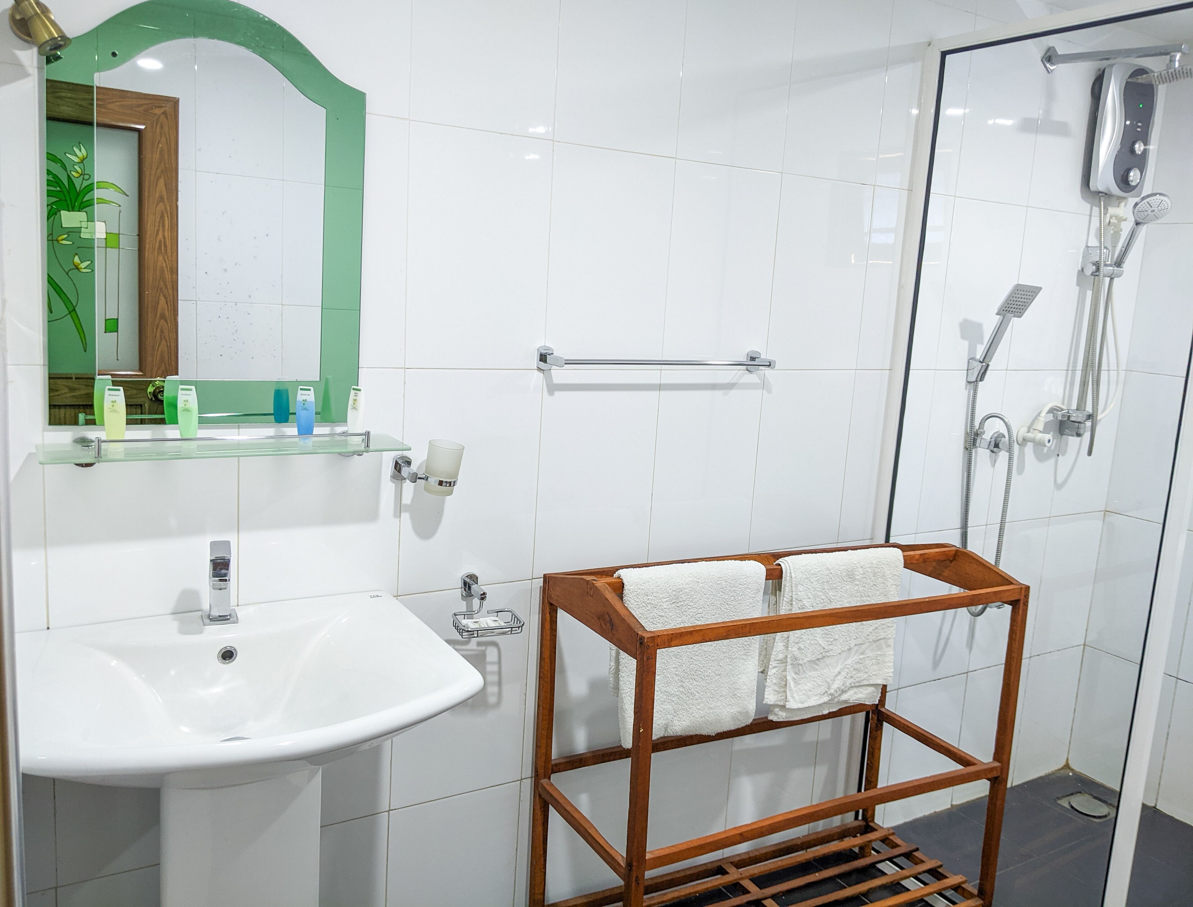 A modern bathroom with a white sink, a glass shower enclosure, and a wooden towel rack.