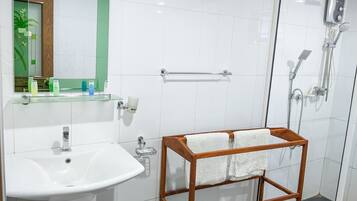 A modern bathroom with a white sink, a glass shower enclosure, and a wooden towel rack.