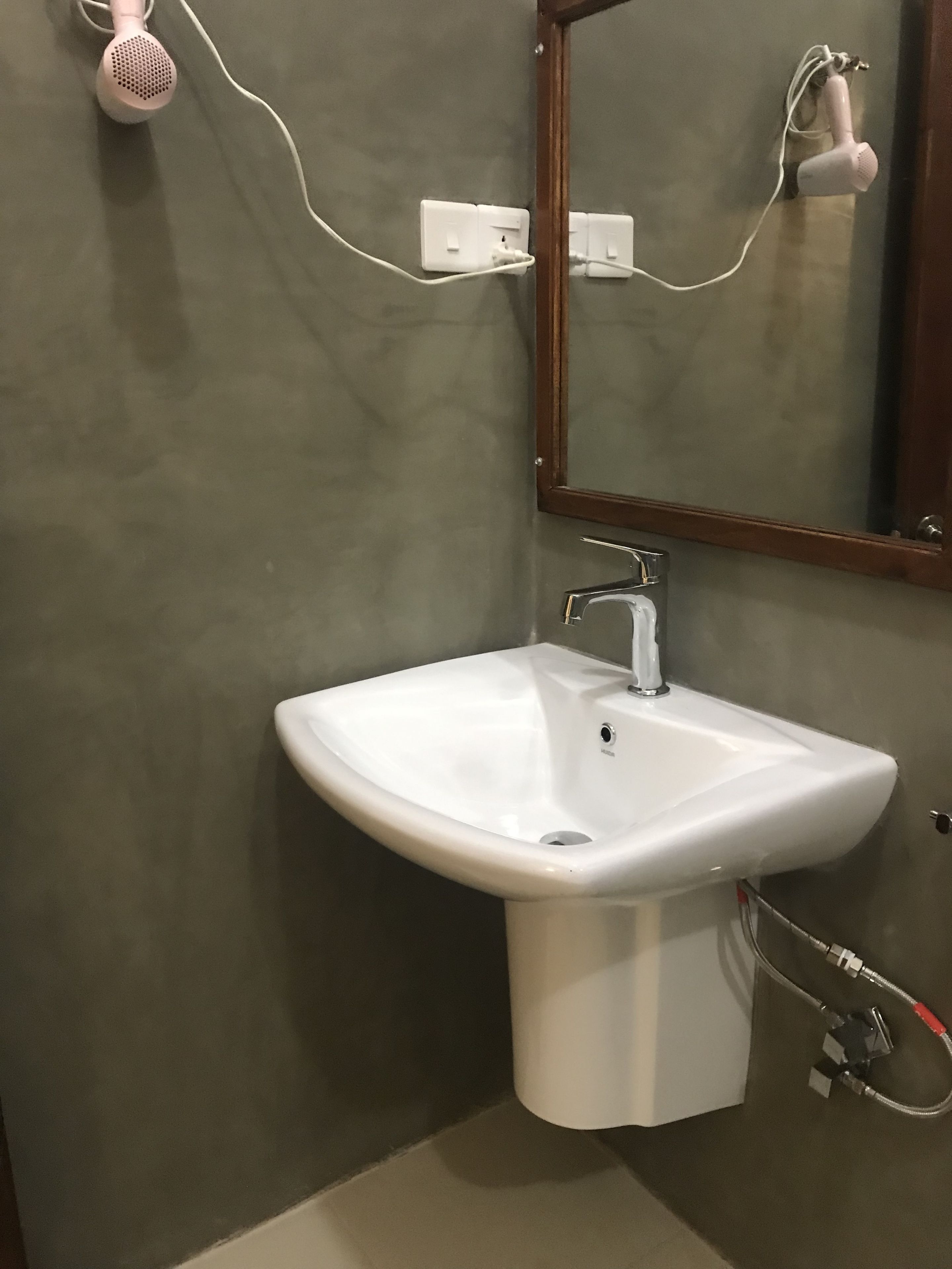 A bathroom with a white pedestal sink, a mirror, and a hairdryer plugged into the wall.