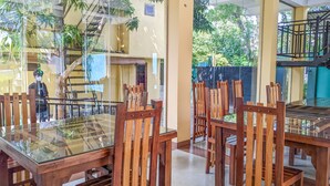 A dining area with glass-top tables and wooden chairs, a staircase, and a view of greenery outside.