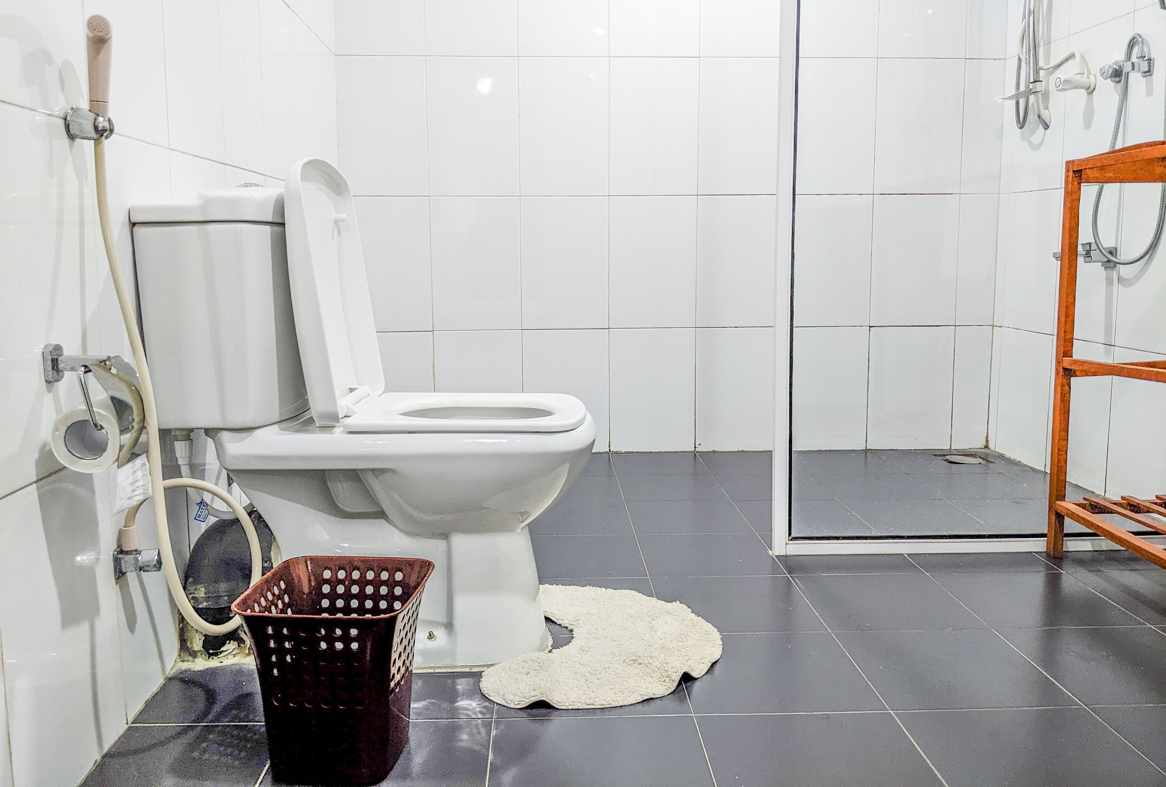 A bathroom with a toilet, a shower, and a wooden shelf.
