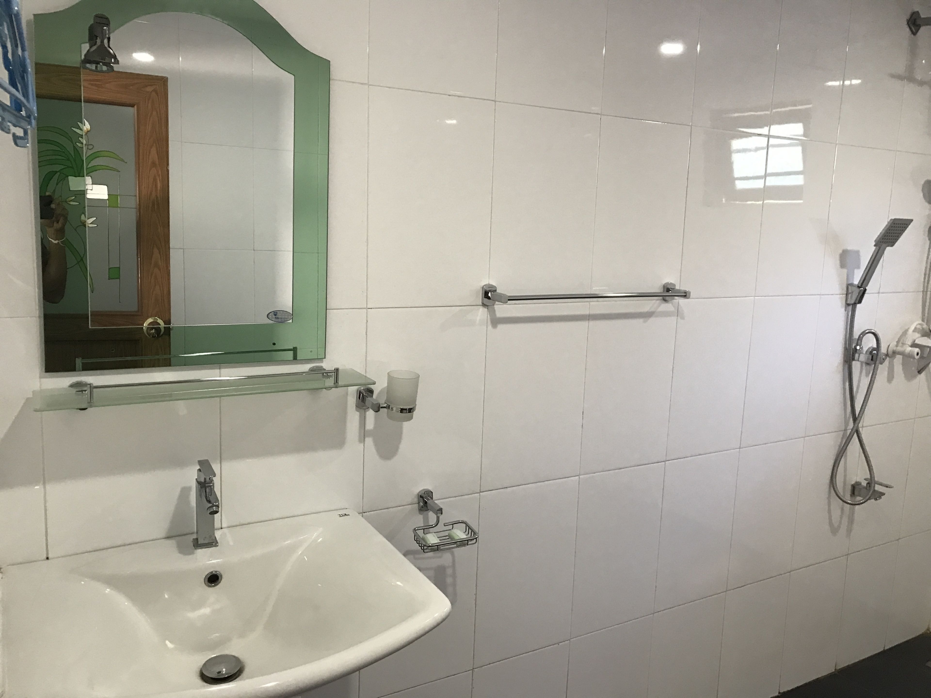 A bathroom with a white sink, a glass shelf, a mirror with a green frame, a towel rack, and a shower area.