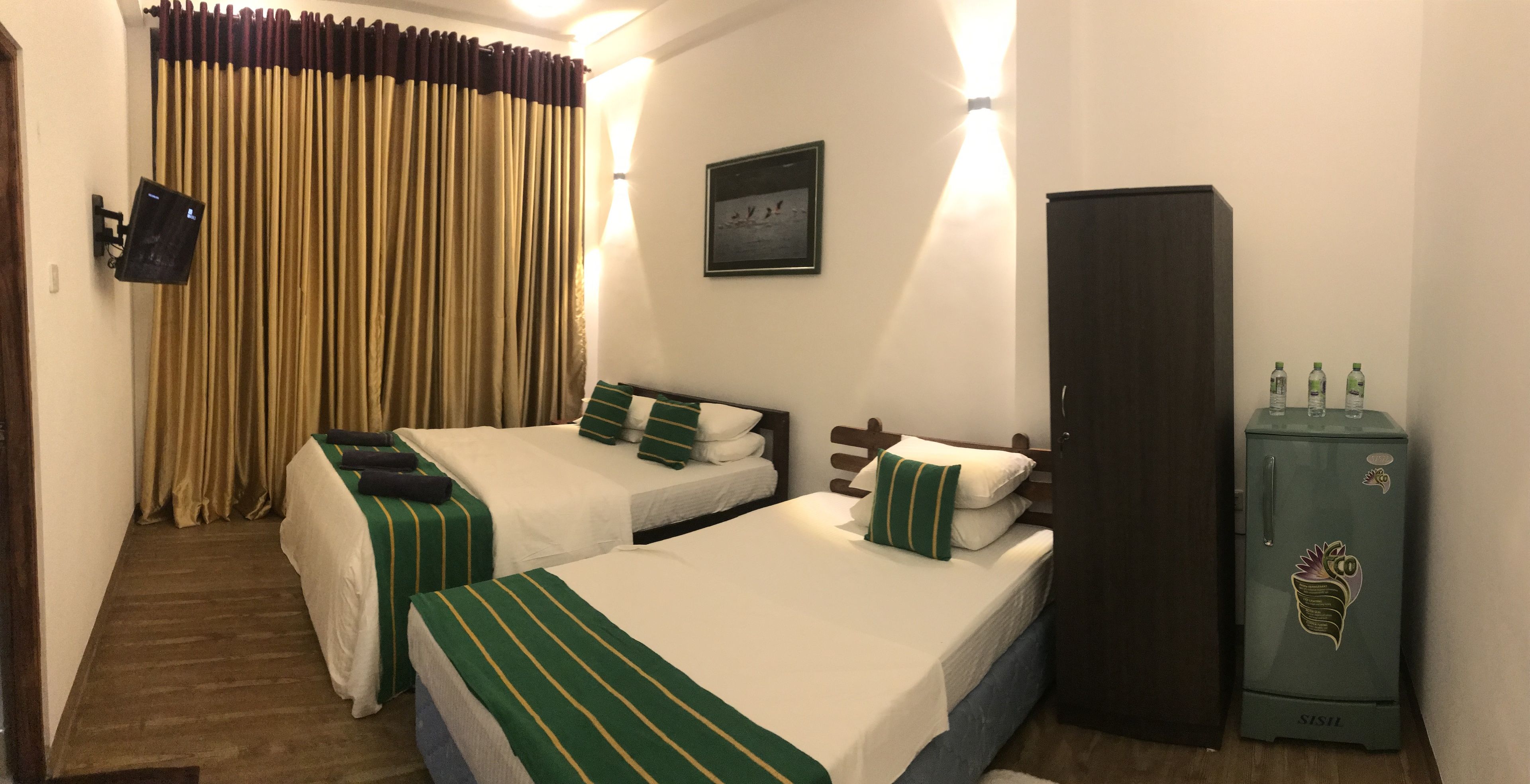 A hotel room with two beds, a minibar, a curtain, and a wall-mounted TV.