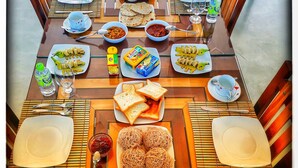 A dining table set with various dishes, including bread, pasta, and vegetables, with chairs around it.