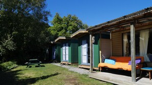 Una cabaña pequeña y rústica con una terraza de madera y una cama individual con ropa de cama colorida.