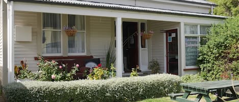 A white building with a porch, a bench, and a table.