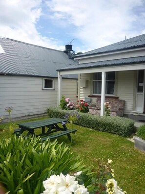 A house with a covered porch, a garden with flowers and a picnic table. - Bon Accord Backpackers (Akaroa)