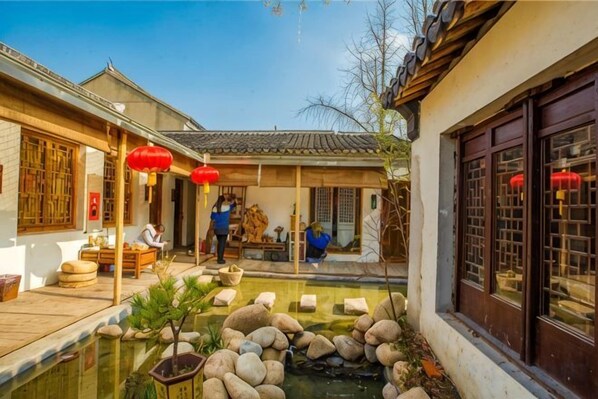 A traditional courtyard with a pond, wooden furniture, and red lanterns. - Memory Home (Suzhou)