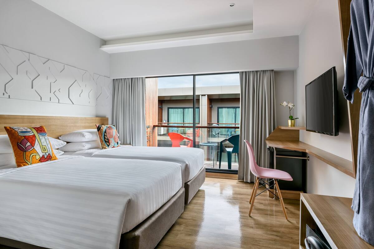 Quarto de hotel com duas camas, uma escrivaninha, televisão e varanda com vista.