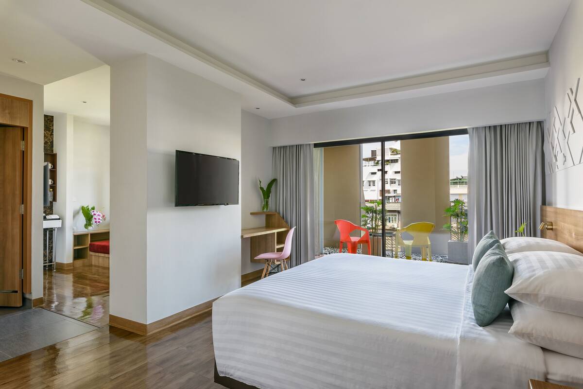 Quarto de hotel com uma cama grande, televisão na parede, escrivaninha com cadeira e varanda com vista para a cidade.