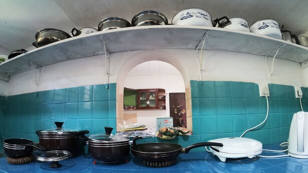 Cuina amb rajoles blaves i blanques, un frigorífic blanc i diferents cassoles i paelles.