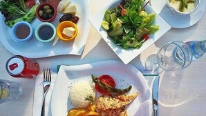 A table with plates of food, including rice, a grilled vegetable, and a slice of pizza. There are also small bowls of condiments and a glass of water. - Kremon Hotel (Usak)