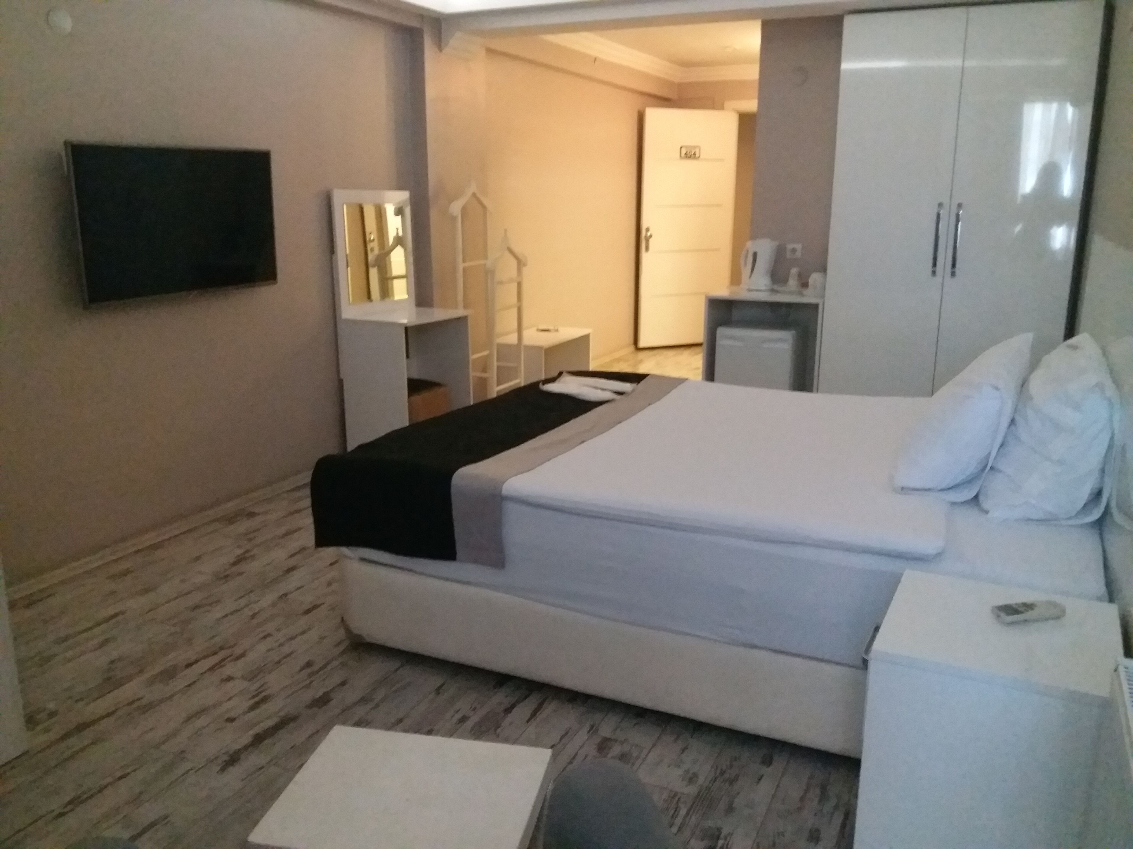 A hotel room with a bed, a bedside table, a wardrobe, a mirror, and a television on the wall.