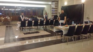 A conference room with tables and chairs, a stage, and a large screen. - Kremon Hotel (Usak)