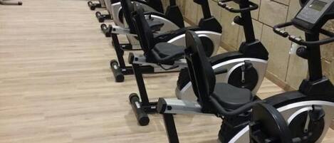 Una fila de bicicletas estáticas en un gimnasio con piso de madera y paredes de piedra.