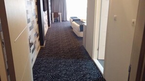 A hallway with patterned carpet leading to a room with a bed and a chair. - Kremon Hotel (Usak)