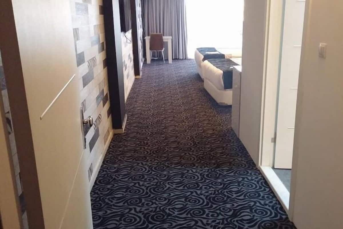 A hallway with patterned carpet leading to a room with a bed and a chair.